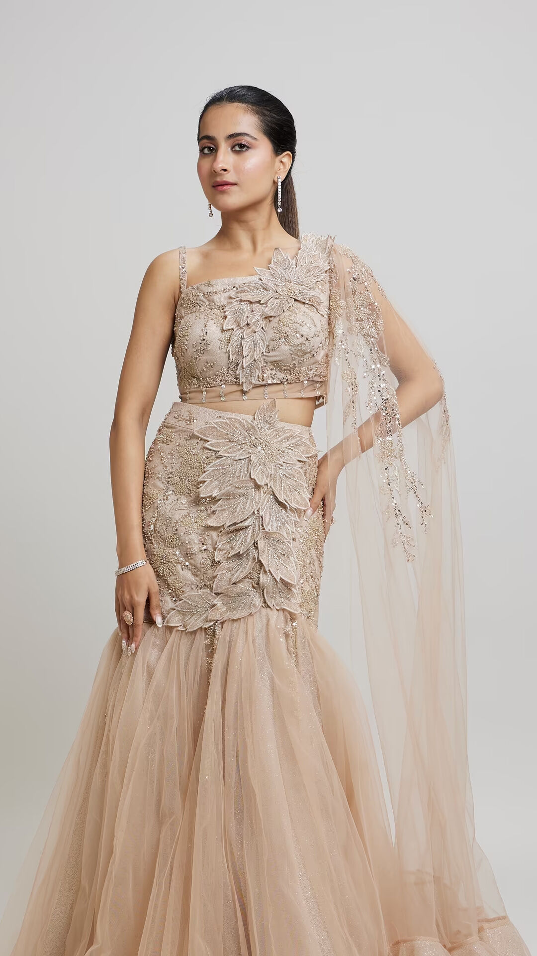 A woman in an elegant golden lehenga with intricate leaf embroidery and a flowing sheer cape.